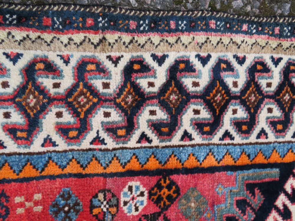 A handwoven Luri tribal rug featuring double geometric diamond medallions in navy blue and red with multi-layered patterned borders. View XII