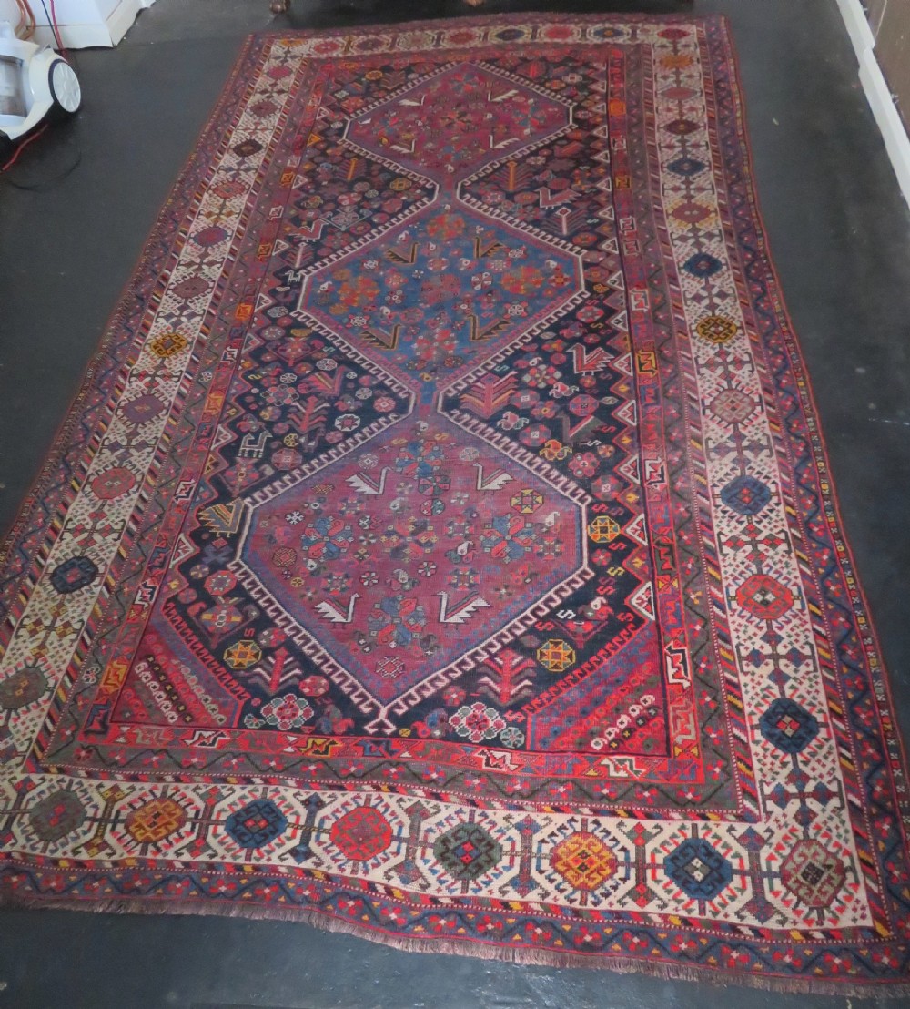 An antique hand-knotted Qashqai wool rug featuring three diamond central medallions with tribal peacock motifs in red, blue, and magenta tones. View II