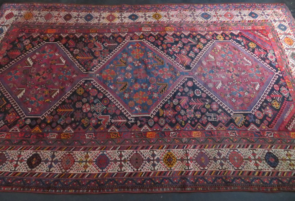 An antique hand-knotted Qashqai wool rug featuring three diamond central medallions with tribal peacock motifs in red, blue, and magenta tones. View V