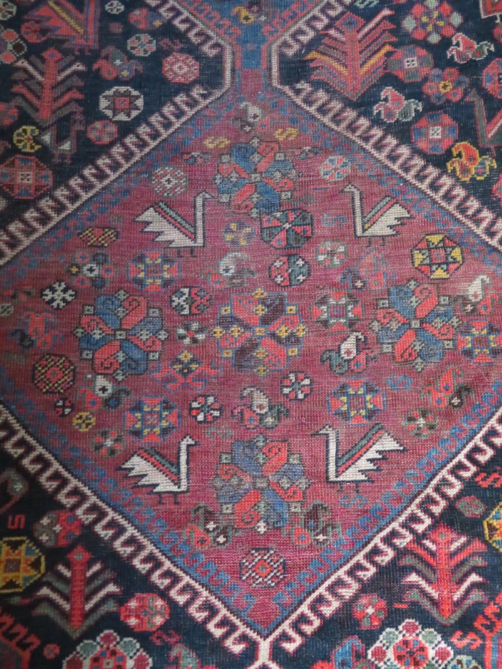 An antique hand-knotted Qashqai wool rug featuring three diamond central medallions with tribal peacock motifs in red, blue, and magenta tones. View VII