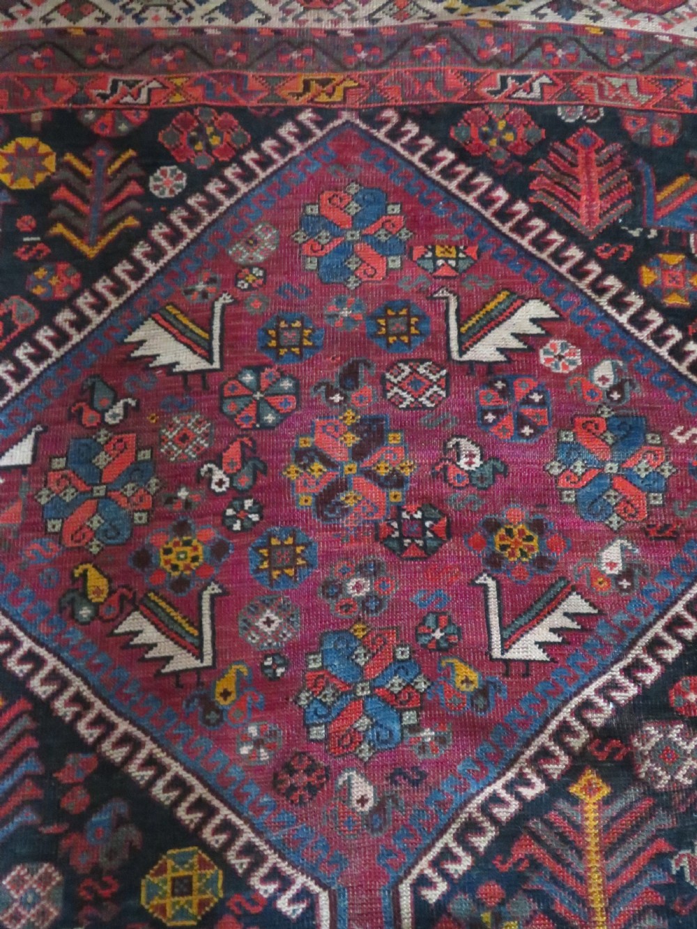 An antique hand-knotted Qashqai wool rug featuring three diamond central medallions with tribal peacock motifs in red, blue, and magenta tones. View IX