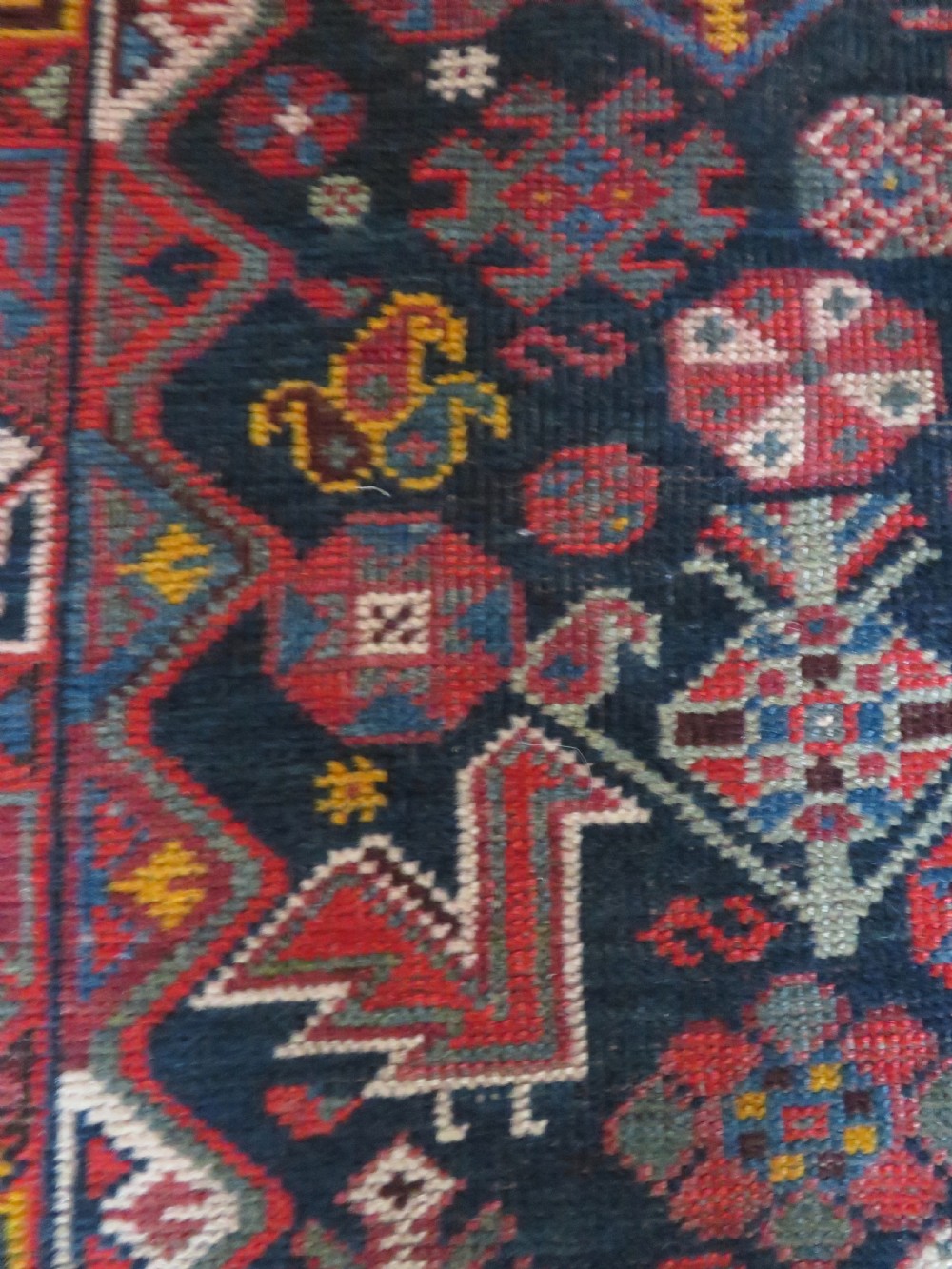An antique hand-knotted Qashqai wool rug featuring three diamond central medallions with tribal peacock motifs in red, blue, and magenta tones. View X
