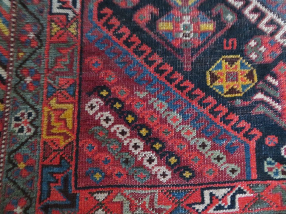 An antique hand-knotted Qashqai wool rug featuring three diamond central medallions with tribal peacock motifs in red, blue, and magenta tones. View XII