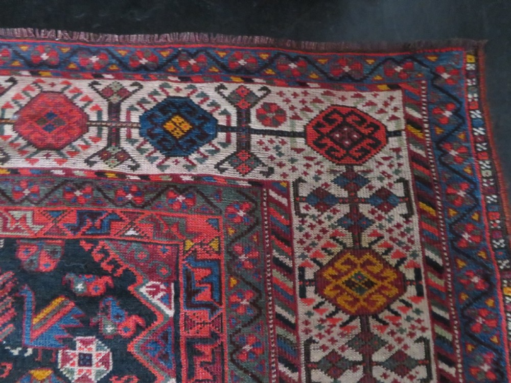 An antique hand-knotted Qashqai wool rug featuring three diamond central medallions with tribal peacock motifs in red, blue, and magenta tones. View XXI