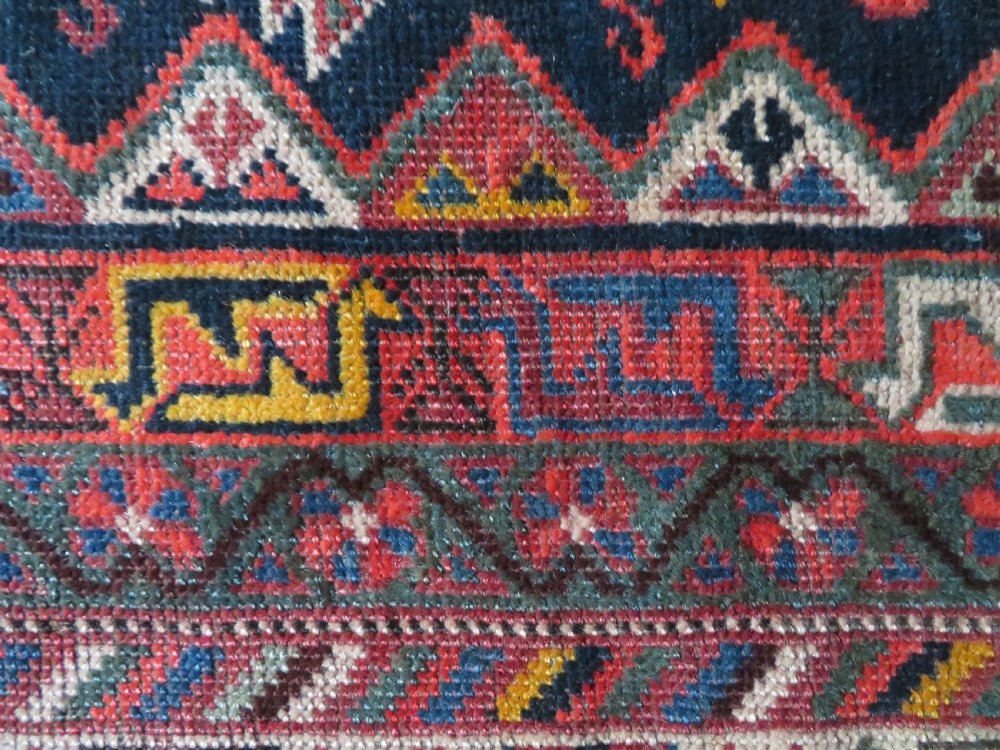 An antique hand-knotted Qashqai wool rug featuring three diamond central medallions with tribal peacock motifs in red, blue, and magenta tones. View XXV