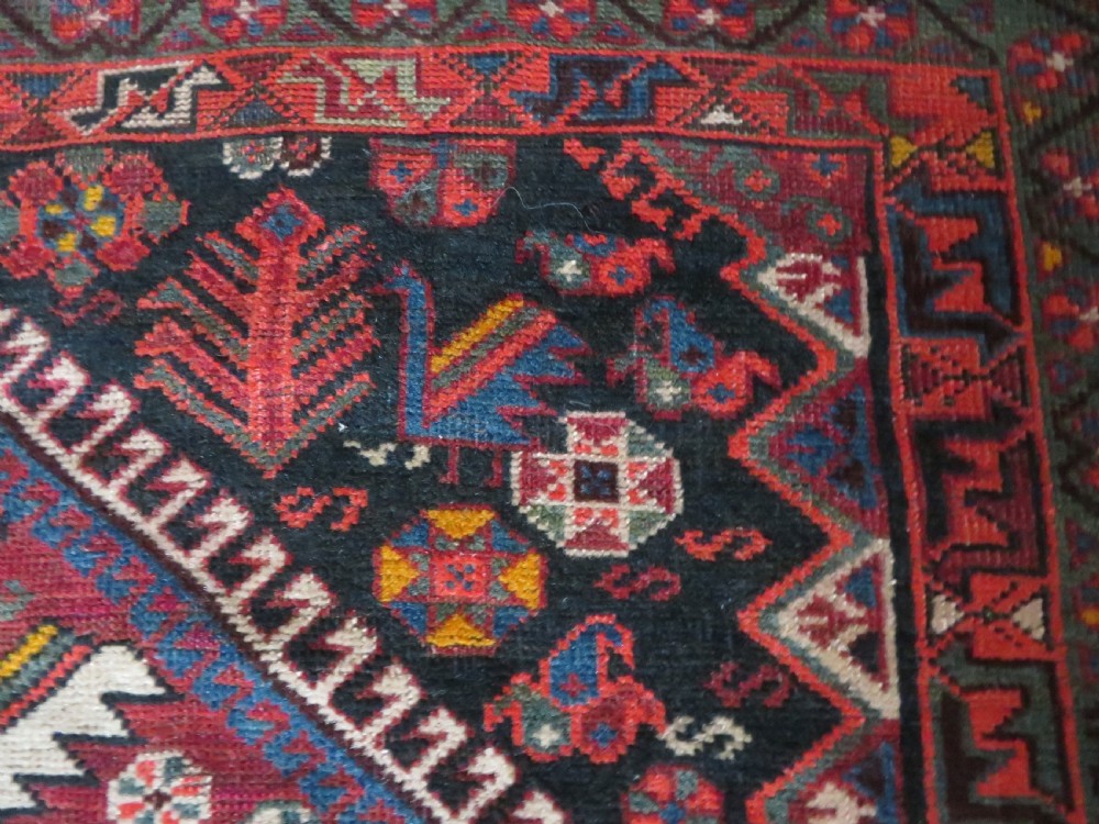 An antique hand-knotted Qashqai wool rug featuring three diamond central medallions with tribal peacock motifs in red, blue, and magenta tones. View XXVII