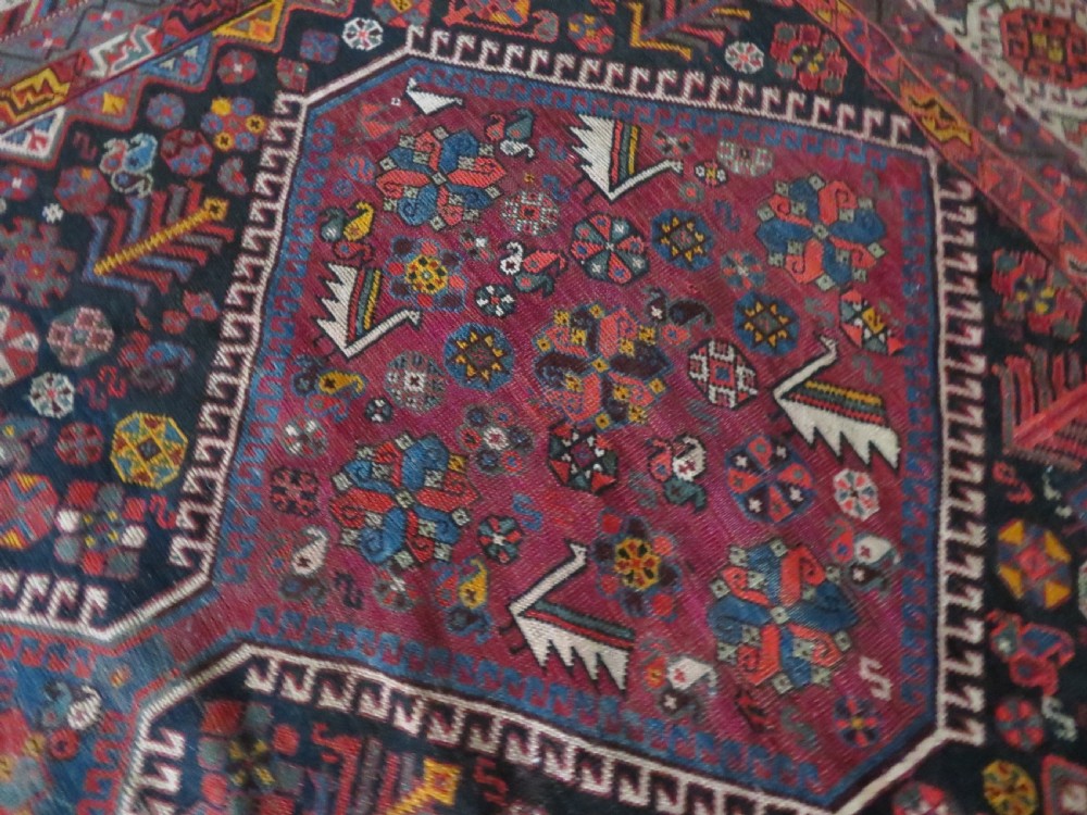 An antique hand-knotted Qashqai wool rug featuring three diamond central medallions with tribal peacock motifs in red, blue, and magenta tones. View XXVIII