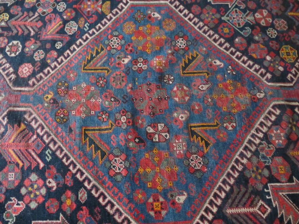 An antique hand-knotted Qashqai wool rug featuring three diamond central medallions with tribal peacock motifs in red, blue, and magenta tones. View XXIX