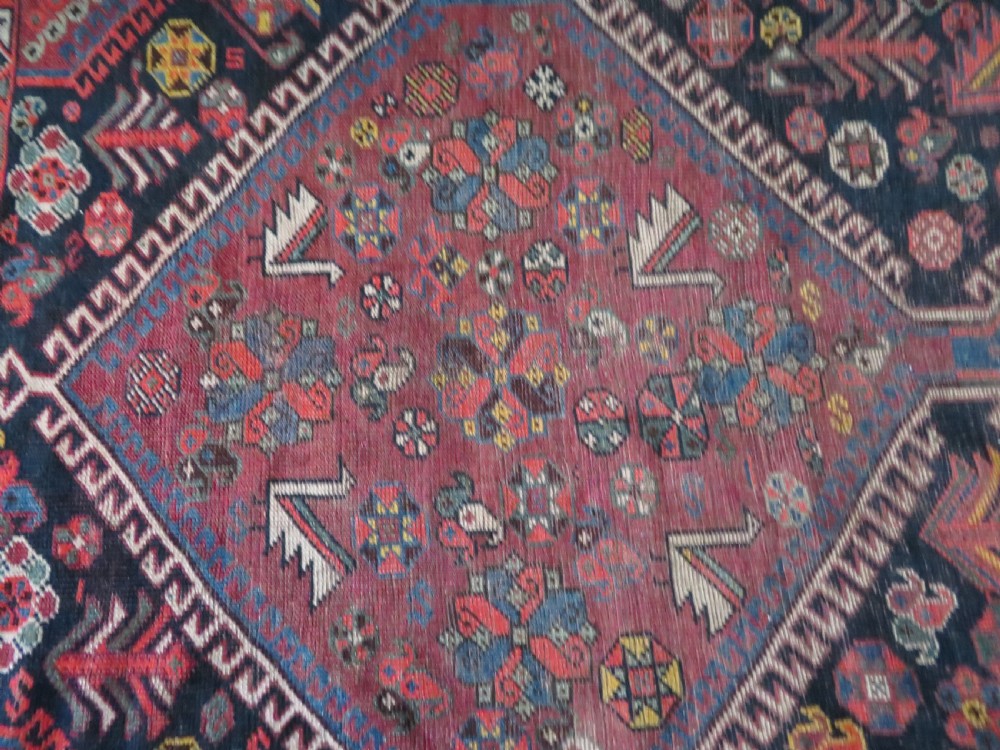An antique hand-knotted Qashqai wool rug featuring three diamond central medallions with tribal peacock motifs in red, blue, and magenta tones. View XXX
