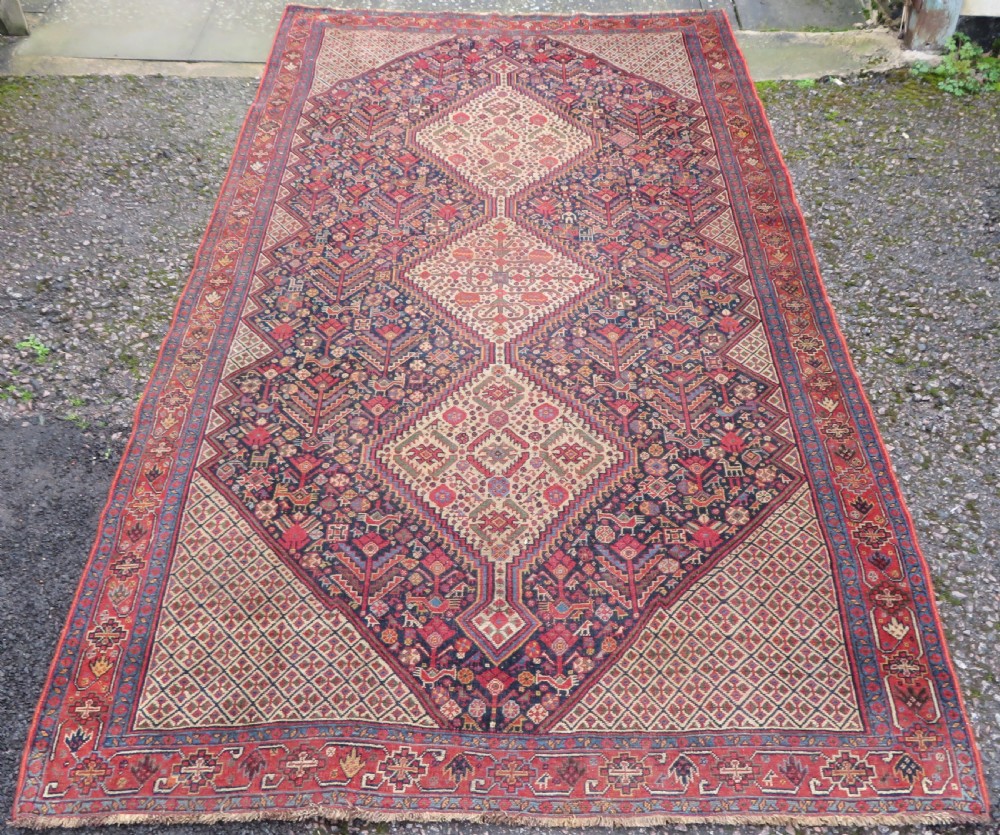 A nineteenth-century hand-knotted Khamseh tribal carpet featuring three diamond-shaped central medallions on an indigo blue field surrounded by geometric borders.