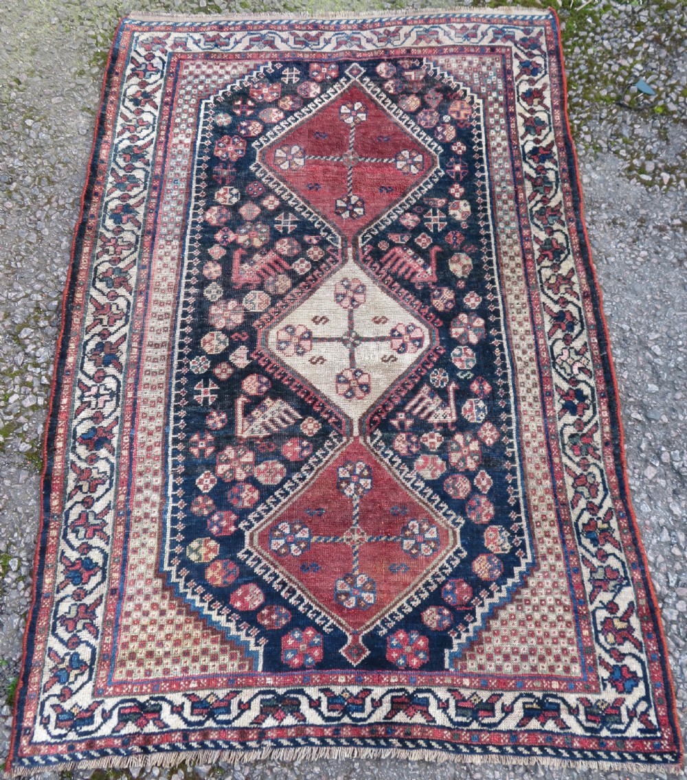 An antique hand-knotted Persian tribal rug featuring three central diamond-shaped medallions, geometric peacock motifs, and multi-layered borders in navy blue, red, and ivory wool.