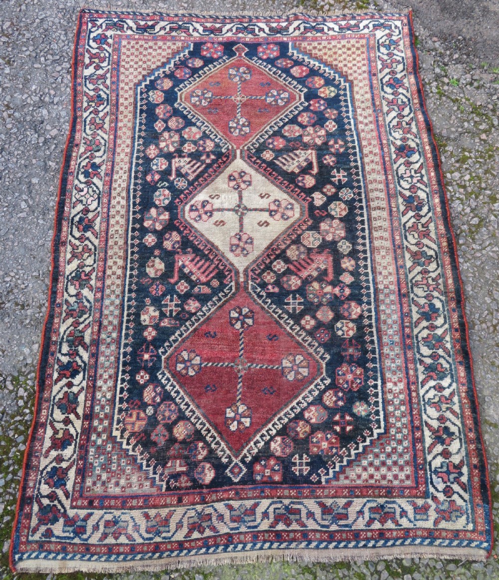 An antique hand-knotted Persian tribal rug featuring three central diamond-shaped medallions, geometric peacock motifs, and multi-layered borders in navy blue, red, and ivory wool. View II