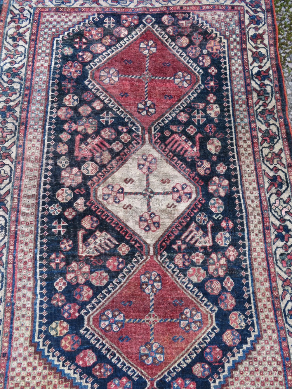 An antique hand-knotted Persian tribal rug featuring three central diamond-shaped medallions, geometric peacock motifs, and multi-layered borders in navy blue, red, and ivory wool. View III