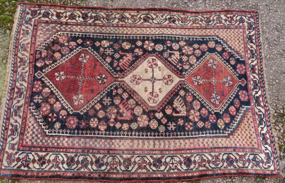 An antique hand-knotted Persian tribal rug featuring three central diamond-shaped medallions, geometric peacock motifs, and multi-layered borders in navy blue, red, and ivory wool. View IV