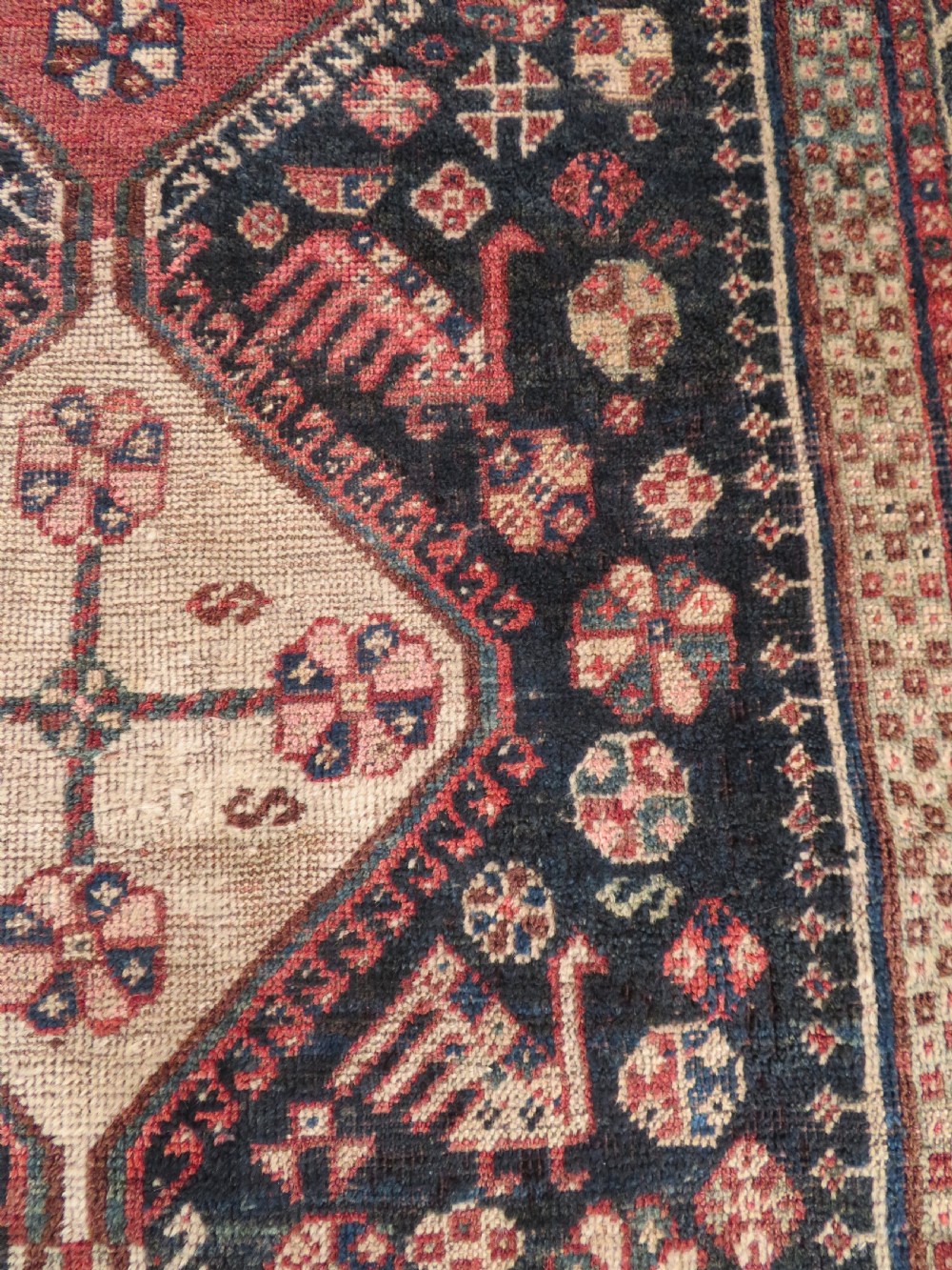 An antique hand-knotted Persian tribal rug featuring three central diamond-shaped medallions, geometric peacock motifs, and multi-layered borders in navy blue, red, and ivory wool. View VII