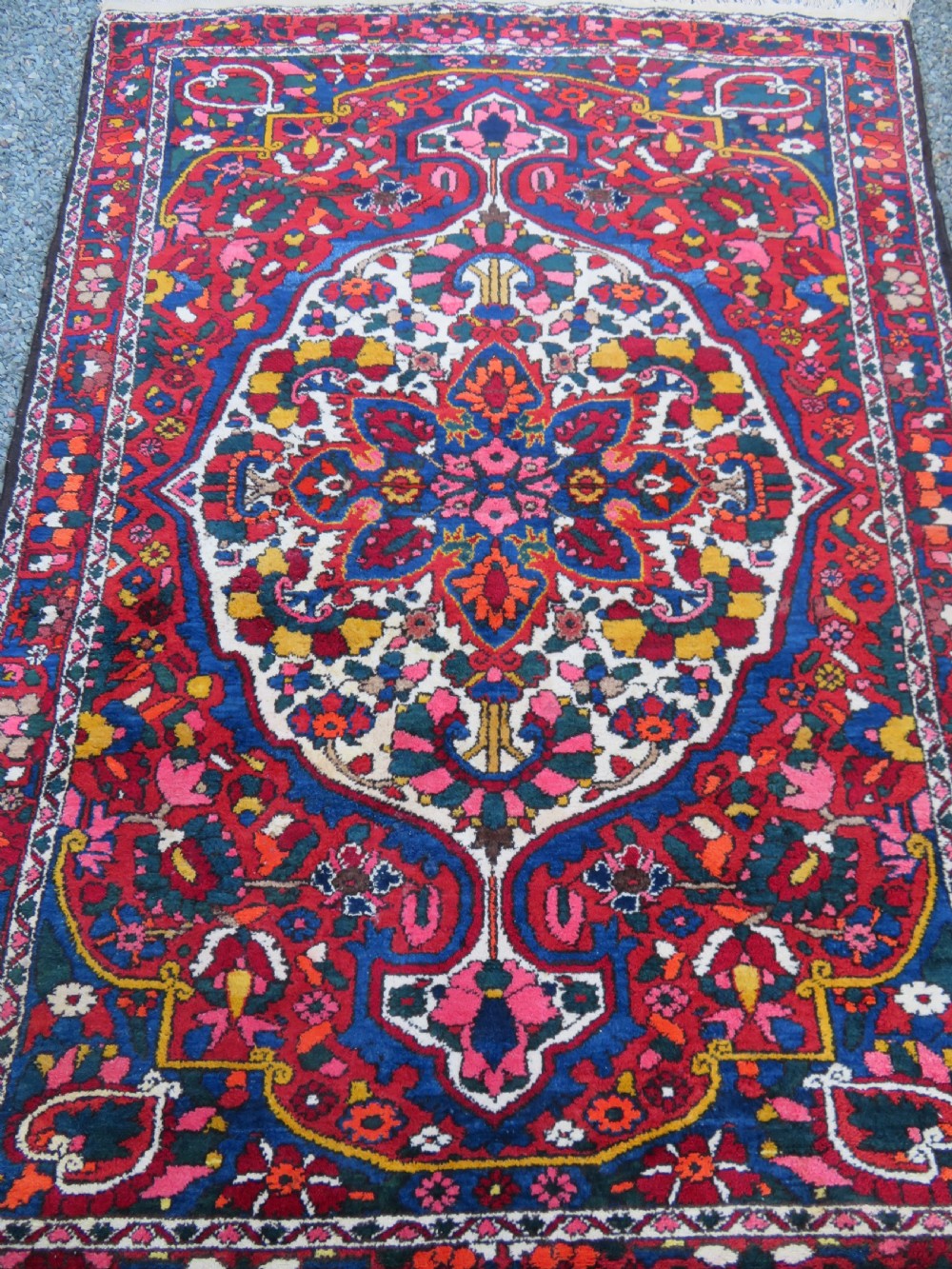 An antique Bakhtiari wool rug featuring a cream and pink central floral medallion framed by red and navy blue fields with complex botanical borders. View III