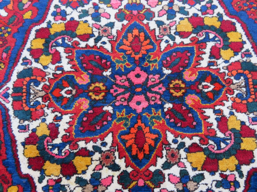 An antique Bakhtiari wool rug featuring a cream and pink central floral medallion framed by red and navy blue fields with complex botanical borders. View IV