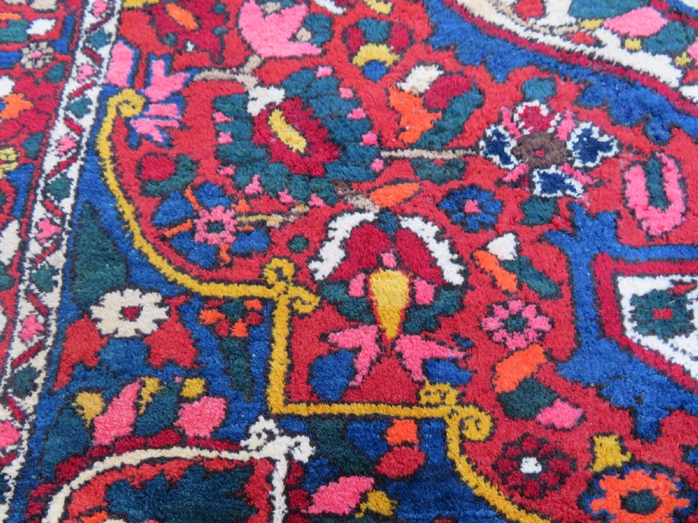 An antique Bakhtiari wool rug featuring a cream and pink central floral medallion framed by red and navy blue fields with complex botanical borders. View VIII