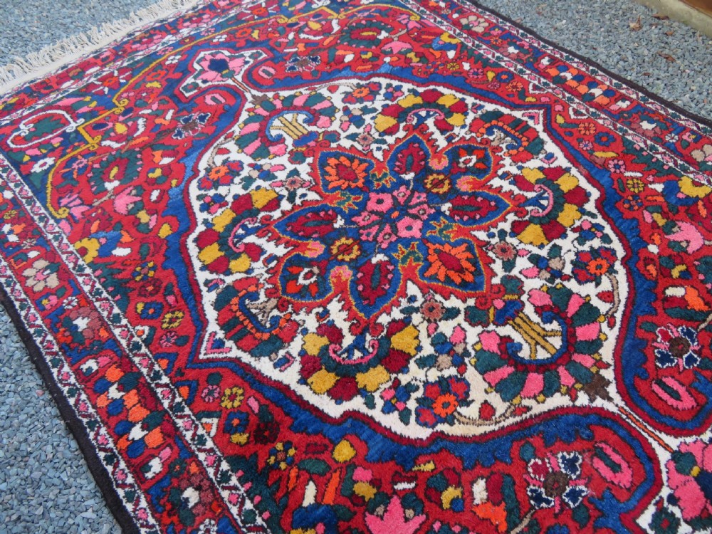 An antique Bakhtiari wool rug featuring a cream and pink central floral medallion framed by red and navy blue fields with complex botanical borders. View XI