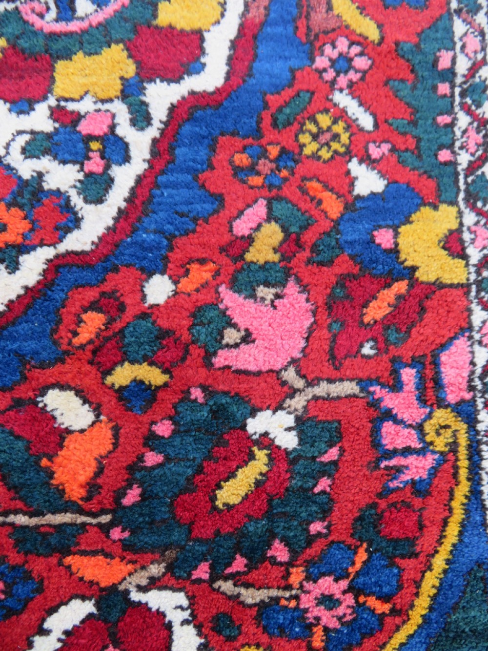 An antique Bakhtiari wool rug featuring a cream and pink central floral medallion framed by red and navy blue fields with complex botanical borders. View XII