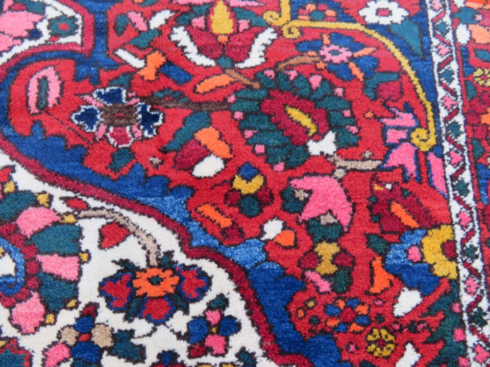 An antique Bakhtiari wool rug featuring a cream and pink central floral medallion framed by red and navy blue fields with complex botanical borders. View XIV