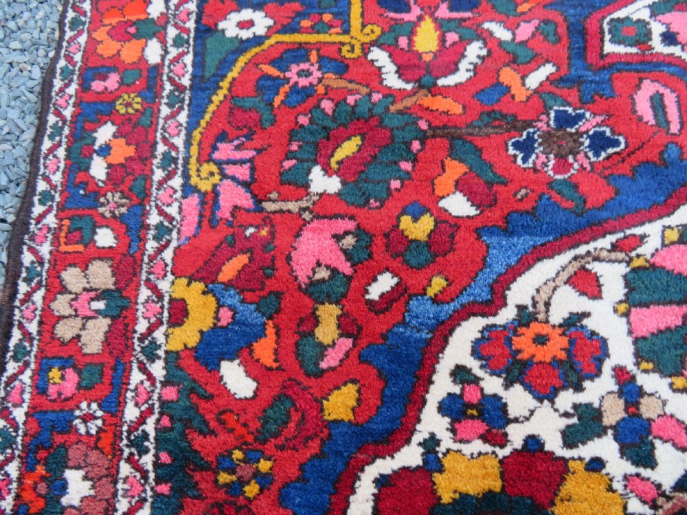 An antique Bakhtiari wool rug featuring a cream and pink central floral medallion framed by red and navy blue fields with complex botanical borders. View XV