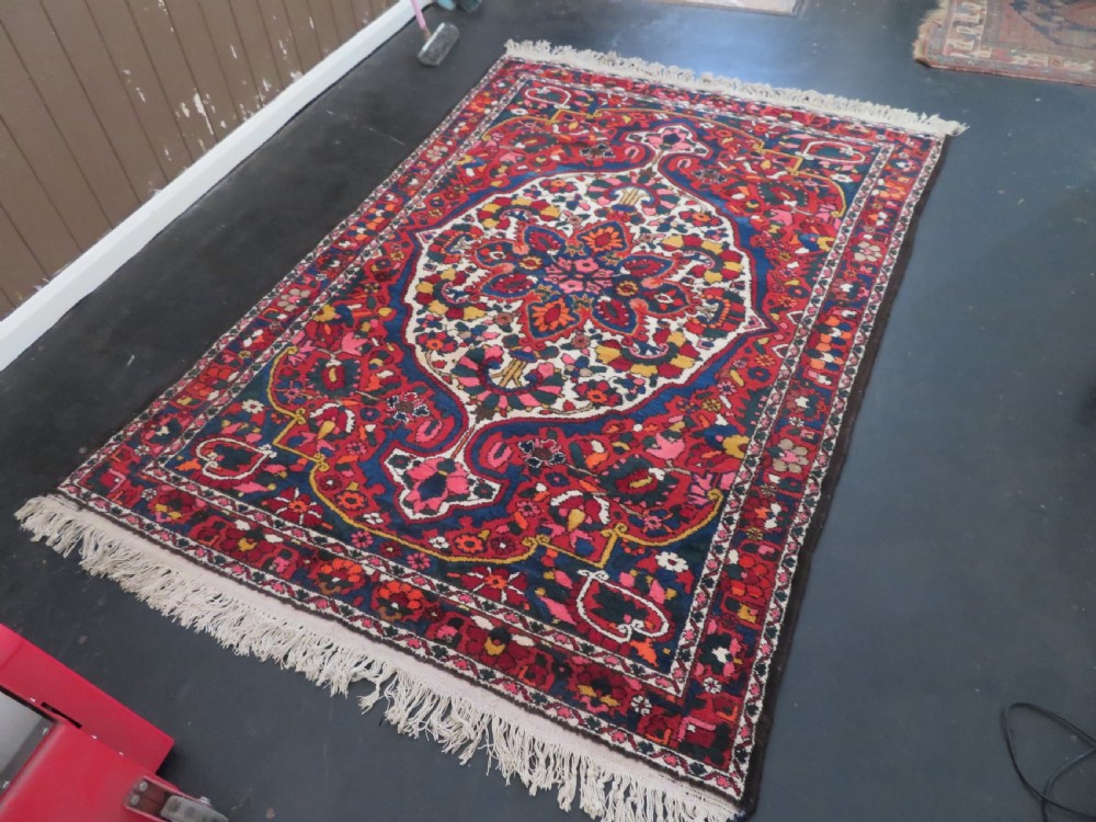 An antique Bakhtiari wool rug featuring a cream and pink central floral medallion framed by red and navy blue fields with complex botanical borders. View XXIII