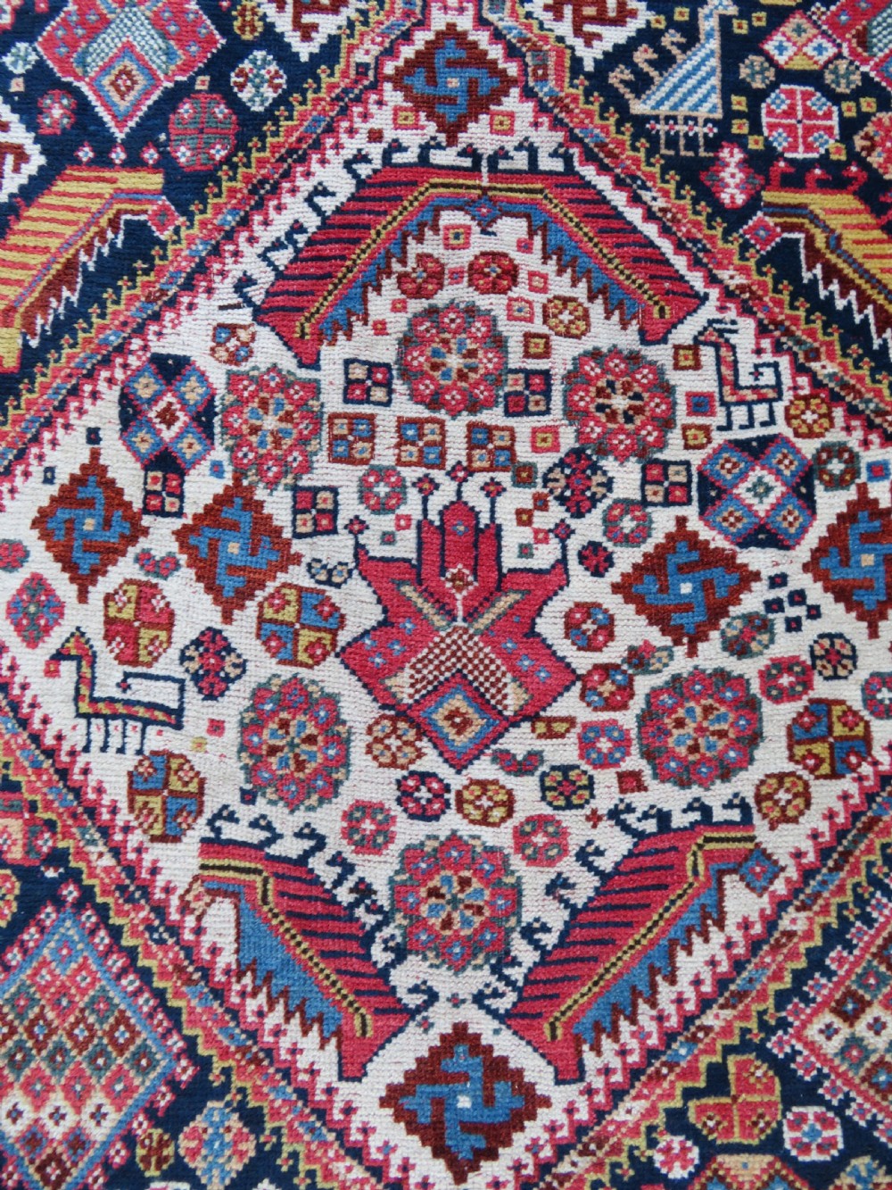 An antique hand-knotted Qashqai Kashkuli wool rug featuring three stacked diamond medallions in red, indigo blue, and ivory surrounded by intricate geometric borders. View IV