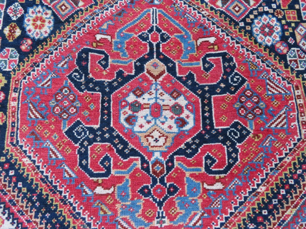 An antique hand-knotted Qashqai Kashkuli wool rug featuring three stacked diamond medallions in red, indigo blue, and ivory surrounded by intricate geometric borders. View VI