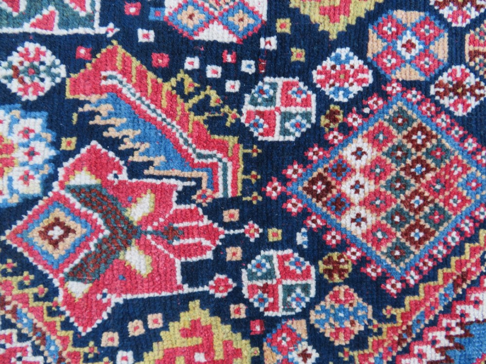 An antique hand-knotted Qashqai Kashkuli wool rug featuring three stacked diamond medallions in red, indigo blue, and ivory surrounded by intricate geometric borders. View VII