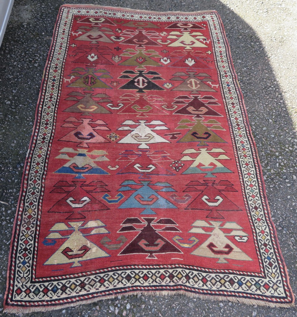 An antique South Caucasian Karabagh hand-knotted wool rug with repeating geometric motifs across a deep red field and a patterned border.