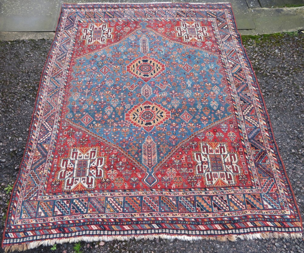 An antique South West Persian Khamseh tribal wool rug featuring a blue central diamond field filled with geometric bird motifs surrounded by a red border.