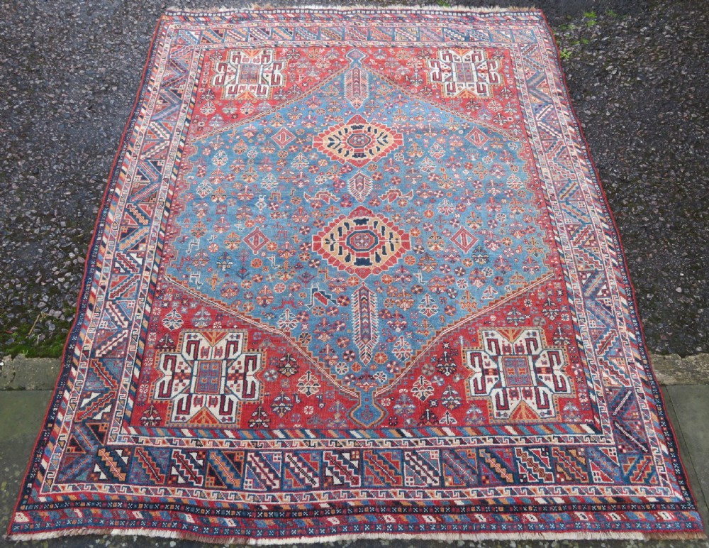 An antique South West Persian Khamseh tribal wool rug featuring a blue central diamond field filled with geometric bird motifs surrounded by a red border. View II