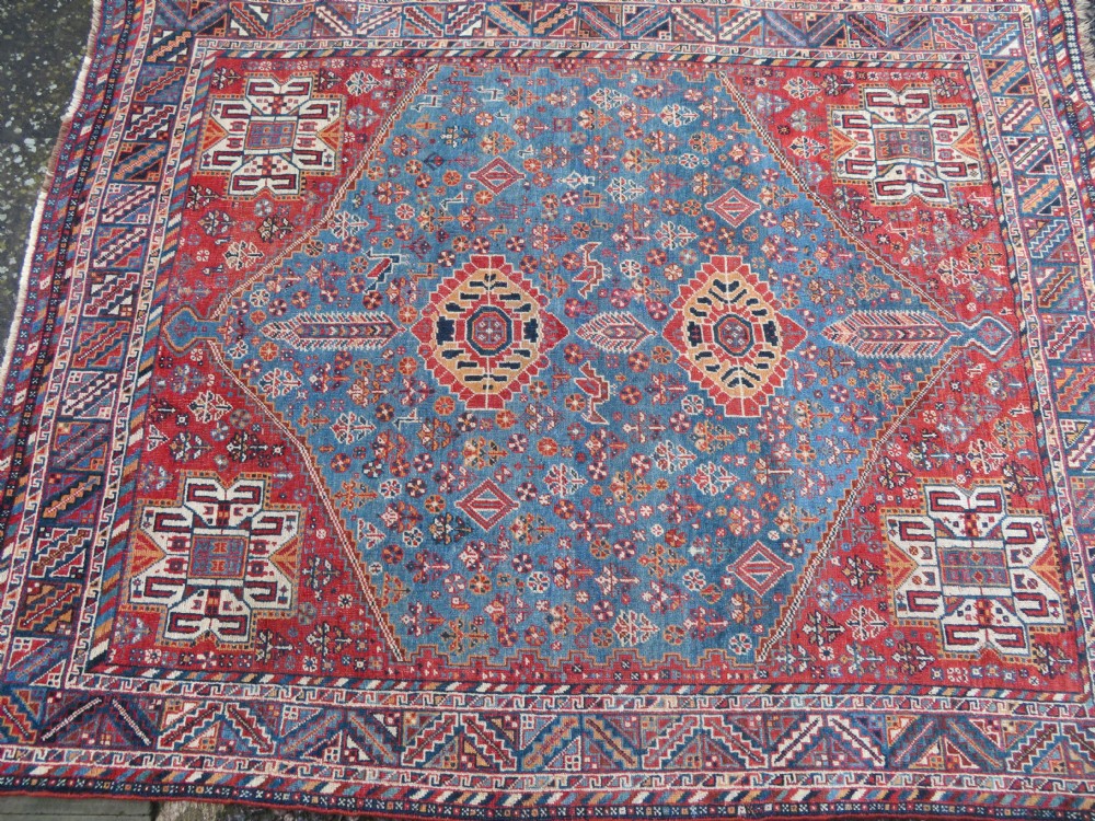 An antique South West Persian Khamseh tribal wool rug featuring a blue central diamond field filled with geometric bird motifs surrounded by a red border. View III
