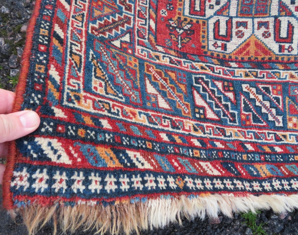 An antique South West Persian Khamseh tribal wool rug featuring a blue central diamond field filled with geometric bird motifs surrounded by a red border. View IV