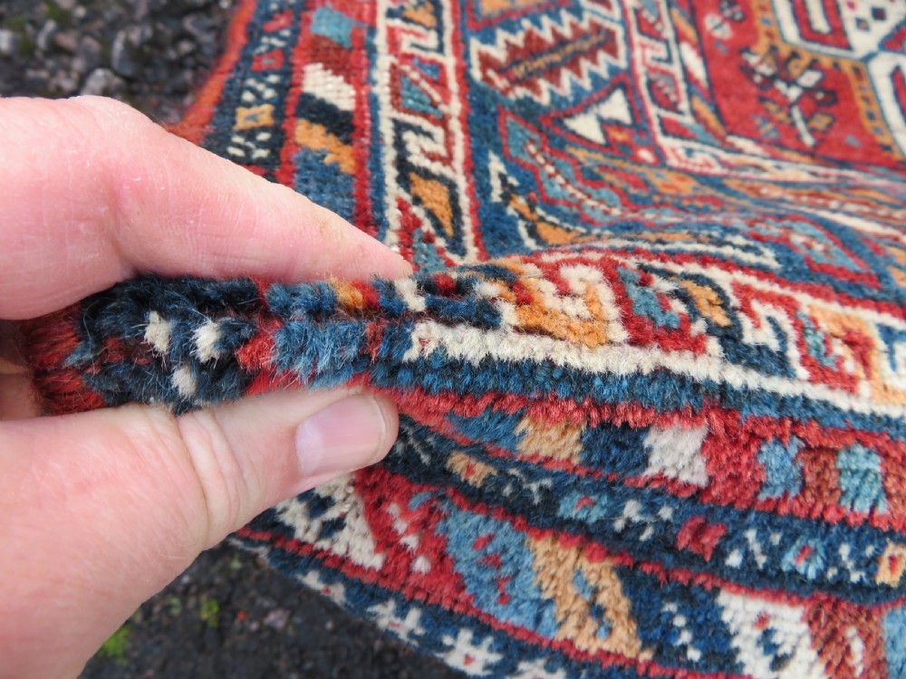 An antique South West Persian Khamseh tribal wool rug featuring a blue central diamond field filled with geometric bird motifs surrounded by a red border. View V
