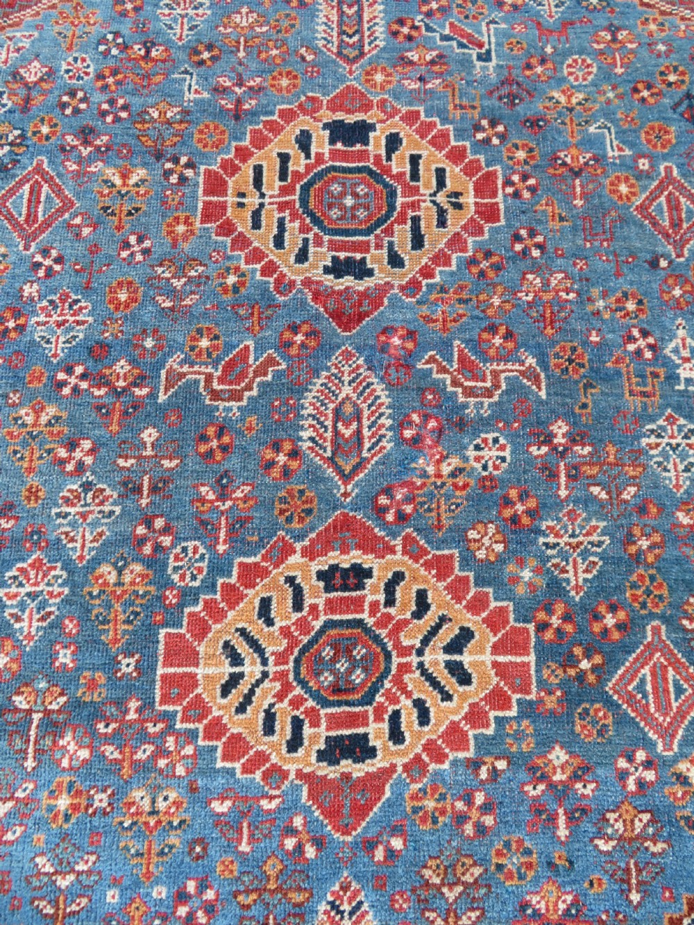 An antique South West Persian Khamseh tribal wool rug featuring a blue central diamond field filled with geometric bird motifs surrounded by a red border. View VI