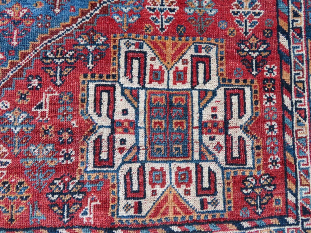 An antique South West Persian Khamseh tribal wool rug featuring a blue central diamond field filled with geometric bird motifs surrounded by a red border. View VII