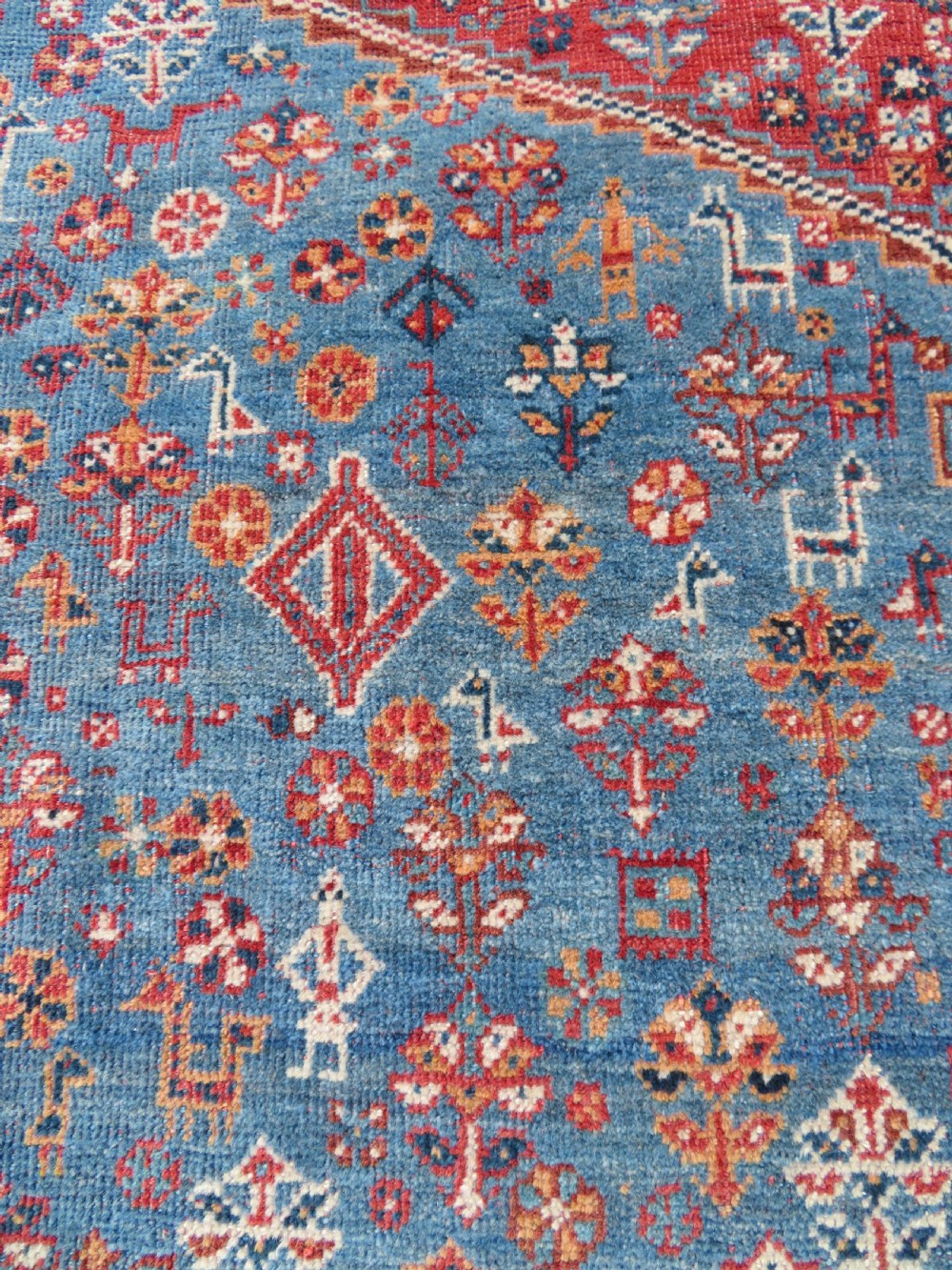 An antique South West Persian Khamseh tribal wool rug featuring a blue central diamond field filled with geometric bird motifs surrounded by a red border. View IX
