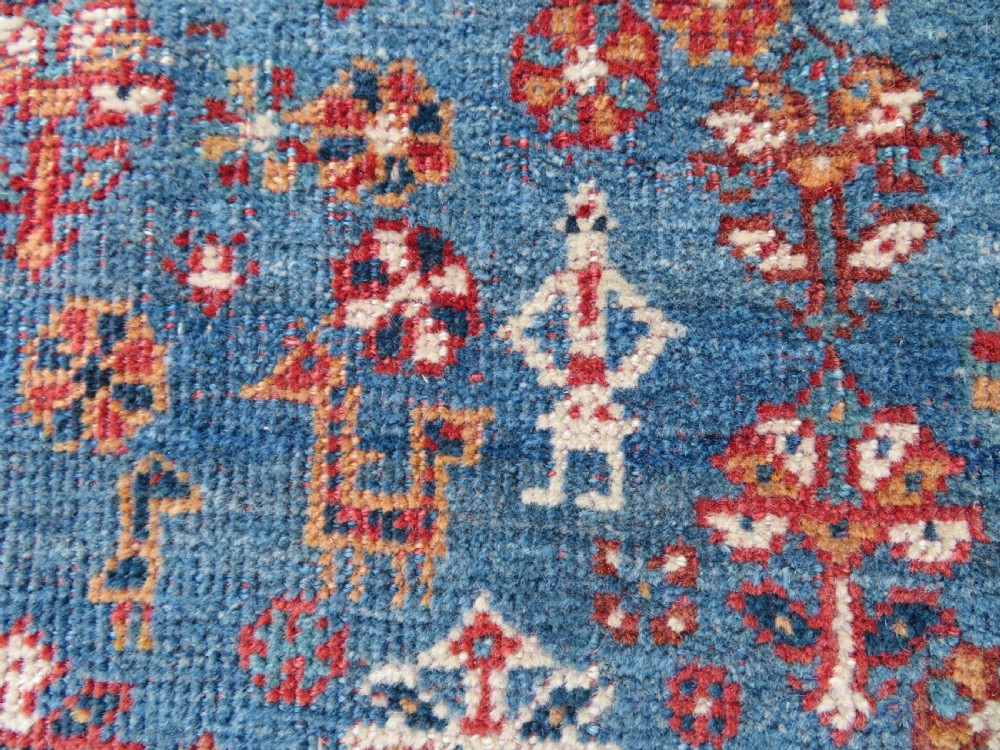 An antique South West Persian Khamseh tribal wool rug featuring a blue central diamond field filled with geometric bird motifs surrounded by a red border. View X