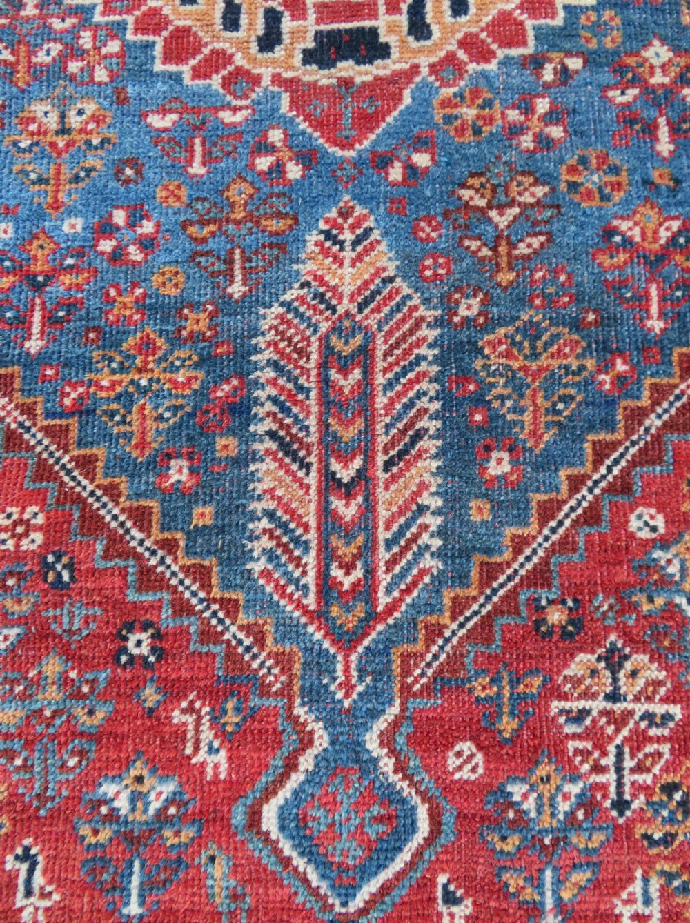 An antique South West Persian Khamseh tribal wool rug featuring a blue central diamond field filled with geometric bird motifs surrounded by a red border. View XII