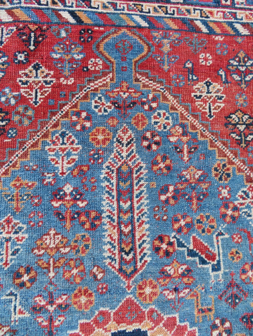An antique South West Persian Khamseh tribal wool rug featuring a blue central diamond field filled with geometric bird motifs surrounded by a red border. View XIII