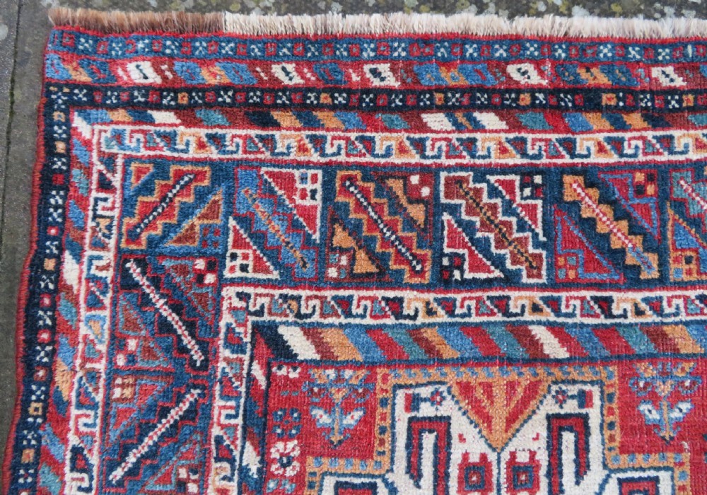 An antique South West Persian Khamseh tribal wool rug featuring a blue central diamond field filled with geometric bird motifs surrounded by a red border. View XIV