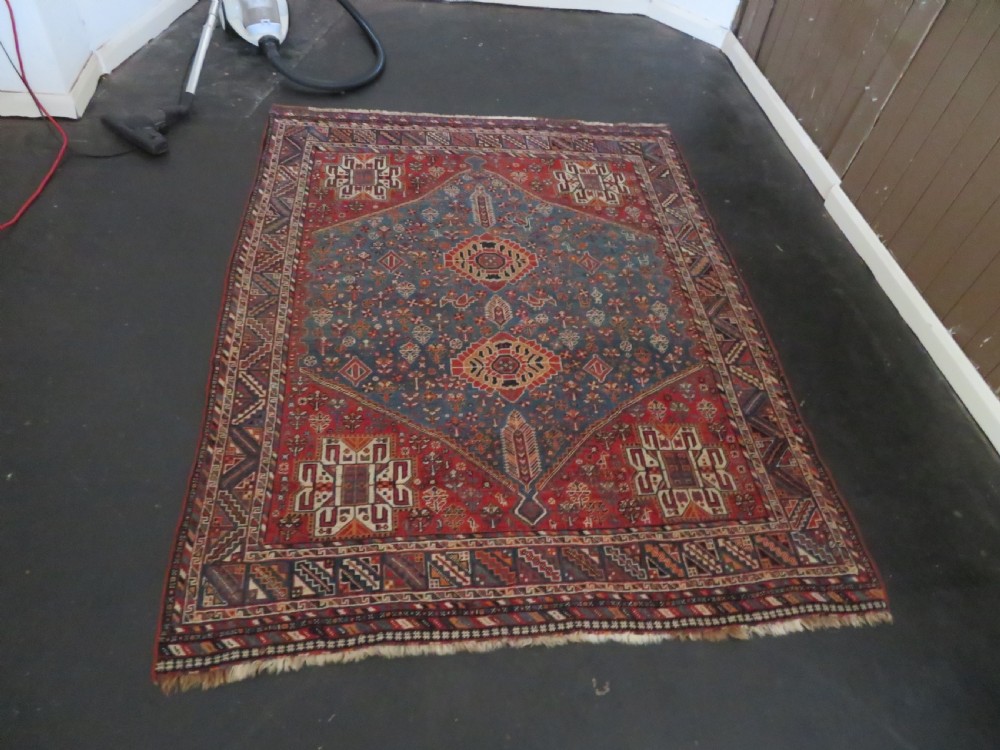 An antique South West Persian Khamseh tribal wool rug featuring a blue central diamond field filled with geometric bird motifs surrounded by a red border. View XIX