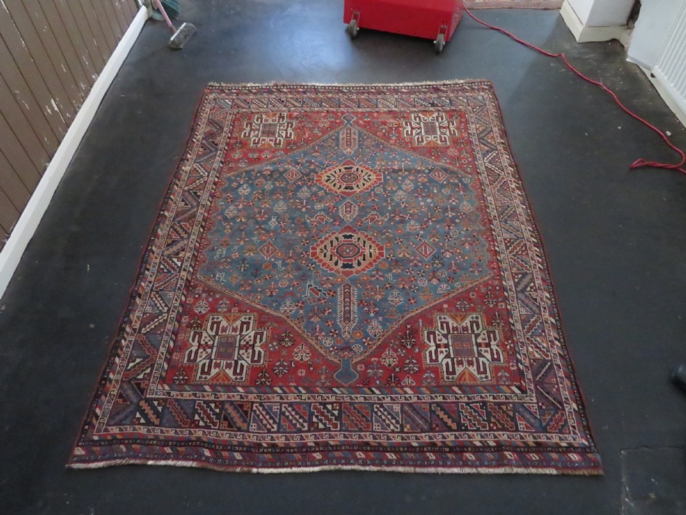 An antique South West Persian Khamseh tribal wool rug featuring a blue central diamond field filled with geometric bird motifs surrounded by a red border. View XX