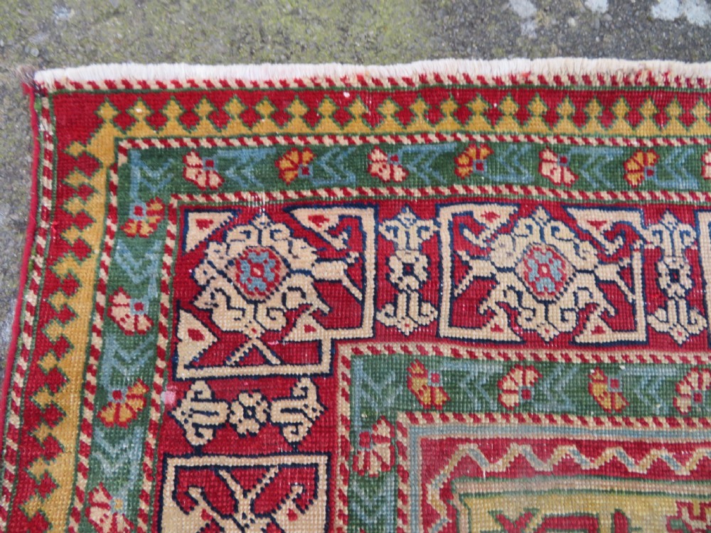 An antique hand-knotted Caucasian rug featuring a distressed yellow central field patterned with geometric ram horn motifs framed by red and green decorative borders. View VI