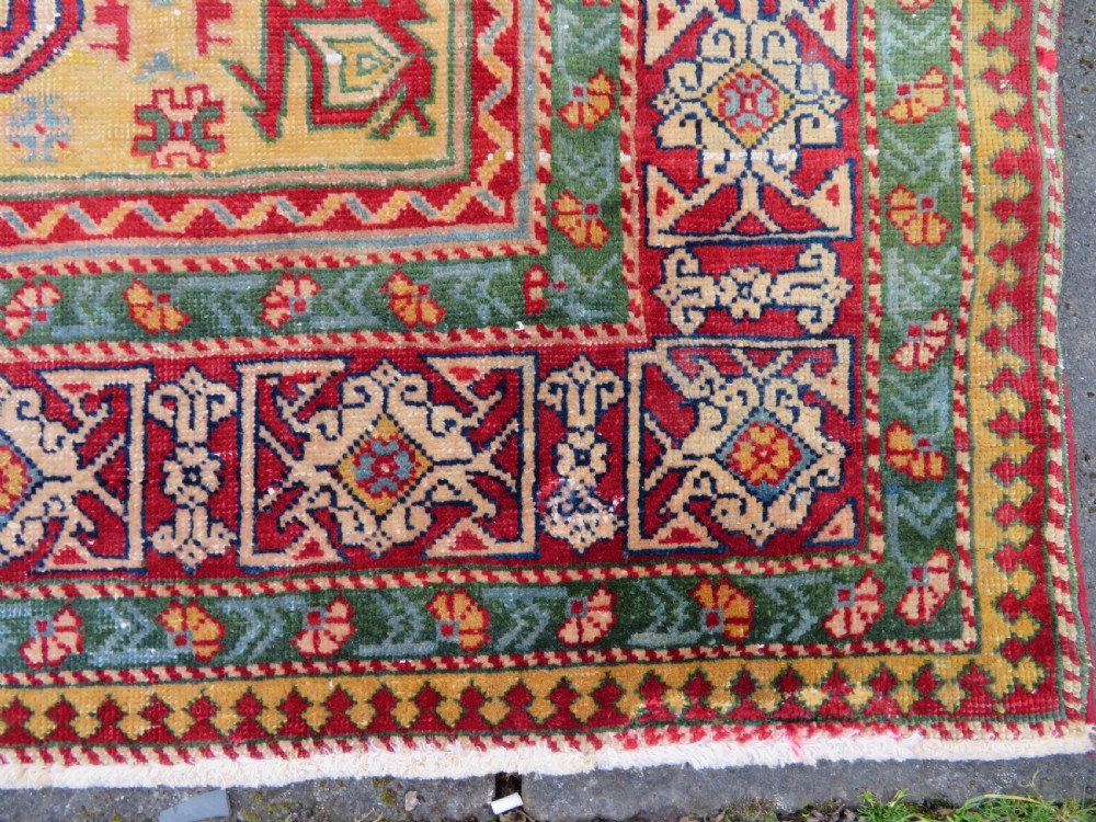 An antique hand-knotted Caucasian rug featuring a distressed yellow central field patterned with geometric ram horn motifs framed by red and green decorative borders. View VIII