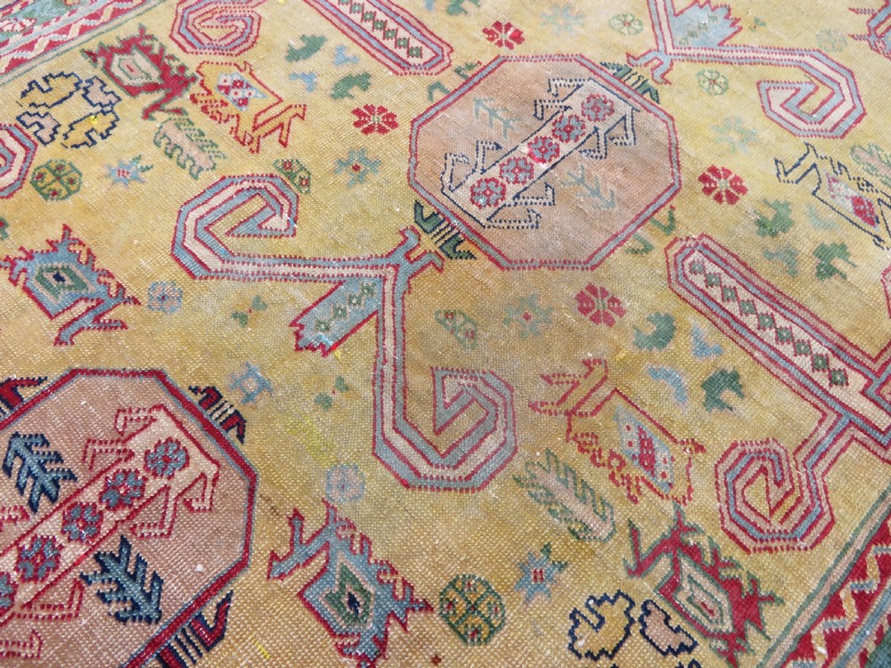 An antique hand-knotted Caucasian rug featuring a distressed yellow central field patterned with geometric ram horn motifs framed by red and green decorative borders. View XI