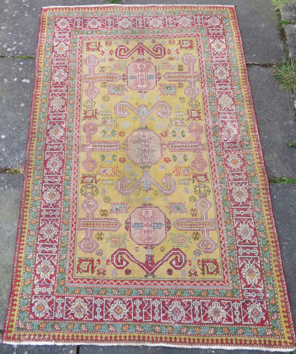 An antique hand-knotted Caucasian rug featuring a distressed yellow central field patterned with geometric ram horn motifs framed by red and green decorative borders. View XIII