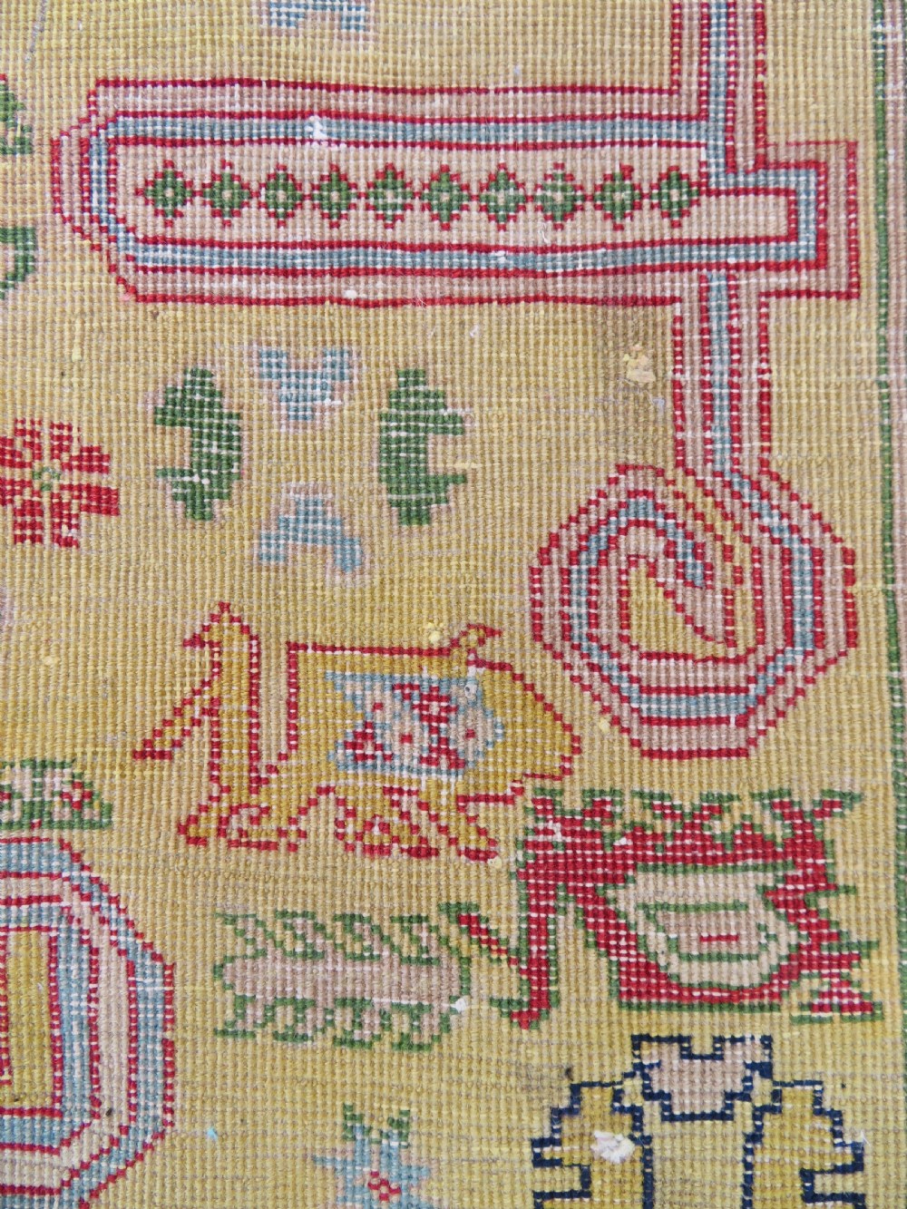 An antique hand-knotted Caucasian rug featuring a distressed yellow central field patterned with geometric ram horn motifs framed by red and green decorative borders. View XIV